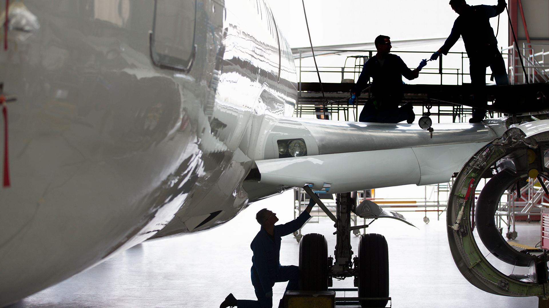 Aircraft technicians working on landing gear and wing inside hangar, showing how aviation MRO software supports maintenance coordination, compliance, and turnaround time.
